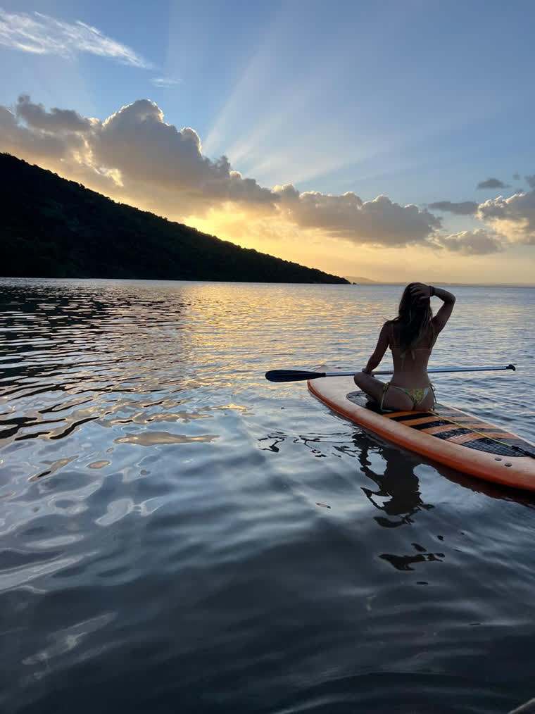 Mulher em uma prancha de stand up paddle observando o pôr do sol no rio